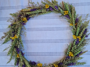 Trockenkranz Ein kunstvoll gestalteter Trockenkranz, verziert mit getrockneten Gräsern, violetten und gelben Blüten, liegt auf einem strukturierten, hellen Untergrund.