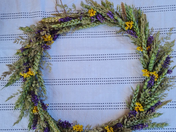 Trockenkranz Ein kunstvoll gestalteter Trockenkranz, verziert mit getrockneten Gräsern, violetten und gelben Blüten, liegt auf einem strukturierten, hellen Untergrund.