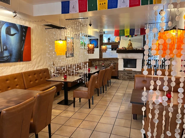 smiling_buddha_gastraum.jpeg Bunt geschmückter Gastraum mit braunen Tischen und Stühlen