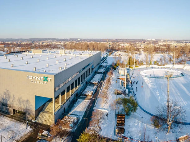 JOYNEXT Arena-1.JPG Große Mehrzweckarena in winterlicher Stadtlandschaft, flankiert von Eisbahn und schneebedeckten Bäumen.