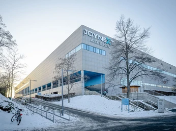 JOYNEXT Arena-6.JPG Moderne Arena im Winter, umgeben von schneebedeckten Gehwegen und kahlen Bäumen.
