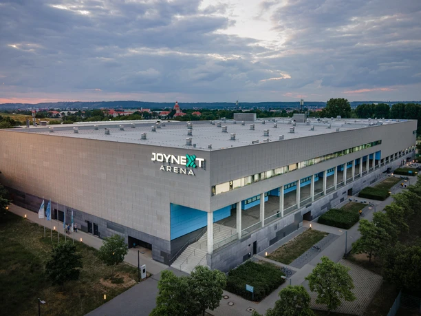 JOYNEXT_Arena - Ansicht SOair - Bild_wunderwaldphoto.com.jpg JOYNEXT Arena bei Dämmerung, modern mit grauer Fassade, umgeben von Bäumen und Spazierwegen.