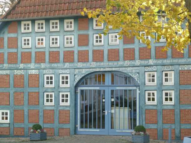 A half-timbered house with a blue facade and reddish-brown bricks, adorned with white windows and carvings.