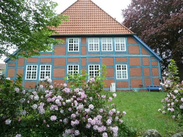 A charming half-timbered house with a red-tiled roof and blooming roses in the foreground.