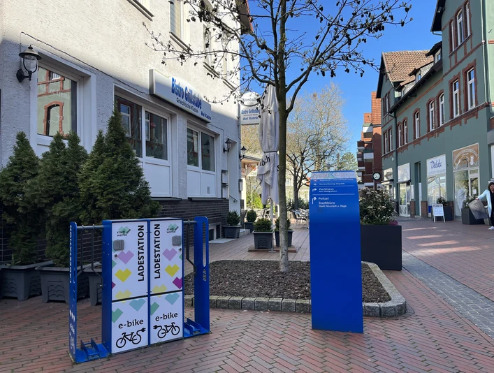 Ladestation für E-Bikes auf einem gepflasterten Platz vor einem Café in einer belebten Einkaufsstraße.
