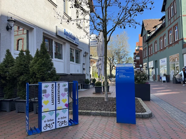 Ladestation Neustadt Ladestation für E-Bikes auf einem gepflasterten Platz vor einem Café in einer belebten Einkaufsstraße.