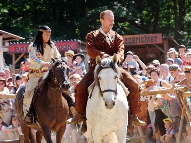 Winnetou 1 der Landesbühnen Sachsen in der Westernstadt.jpg Winnetou-Darsteller und Reiter in Kostümen bei Westernaufführung vor Publikum.