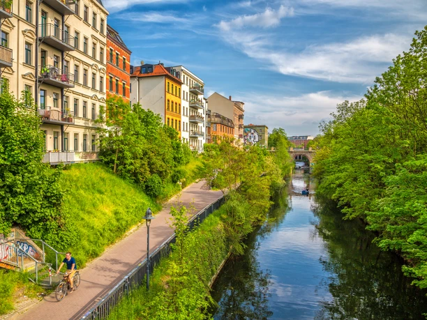 Green trees on the Karl Heine Canal in summer, colorful houses, blue sky, water