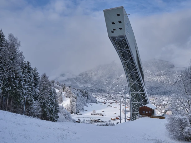 Skisprungschanze Skisprungschanze ragt über verschneites Tal mit Wäldern und verstreuten Häusern.
