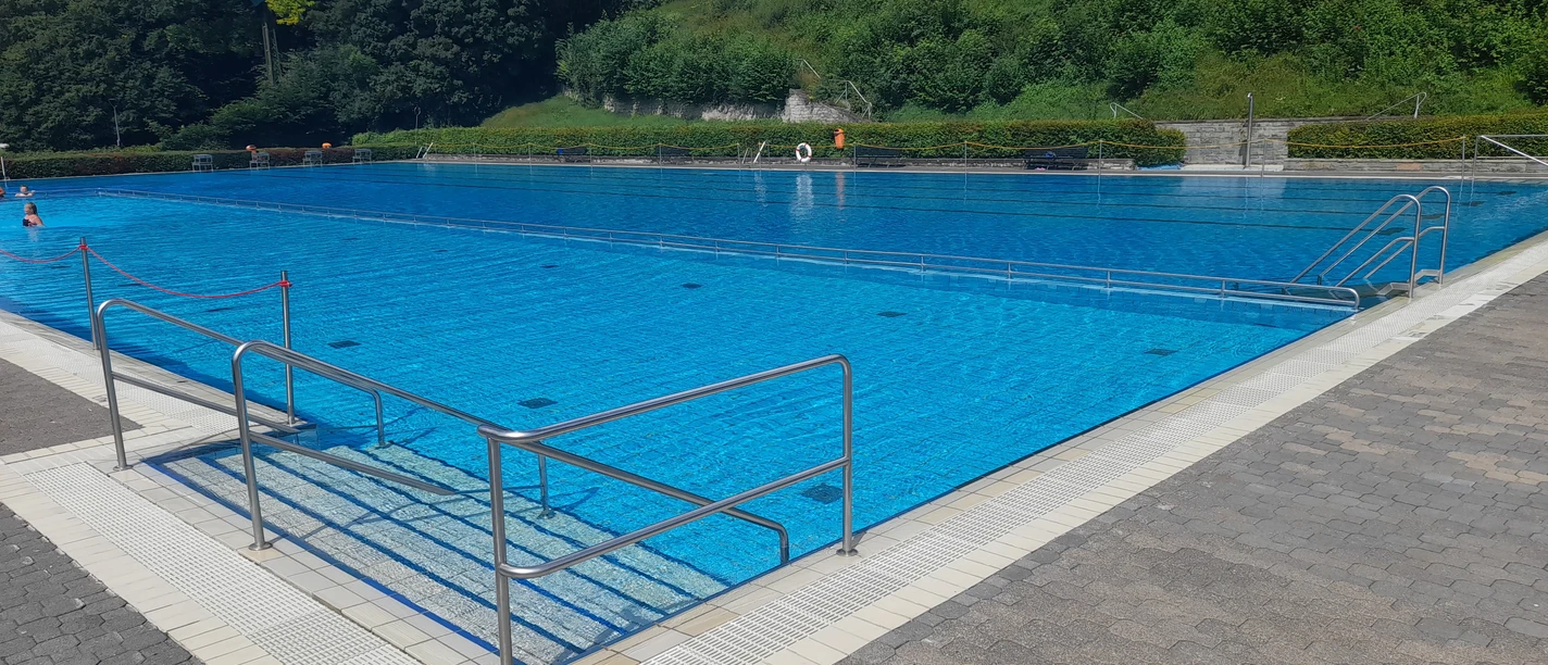 Freibad Büren: Modernes Schwimmbecken umgeben von Grüngürtel und Zugangstreppe am Beckenrand.