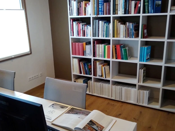 Lesesaal.jpg Moderner Leseraum mit Bücherregal, Schreibtisch, Computer und geöffneten Büchern auf hellem Holzboden