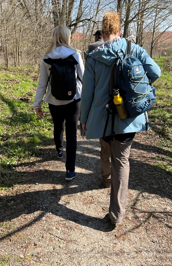 Zwei Personen wandern auf einem sonnigen Waldweg mit Rucksäcken in der Mittelweser-Region.