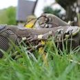 Wanderschuhe Ein Paar braune Wanderschuhe liegt im Gras, umgeben von Blumen, im Hintergrund sind Bäume zu sehen.