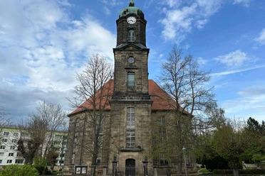 Kirche Lohmen Historic church with a red roof and high clock tower, surrounded by bare trees, against a blue sky with clouds.