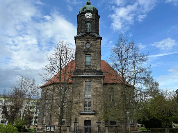Kirche Lohmen Historic church with a red roof and high clock tower, surrounded by bare trees, against a blue sky with clouds.