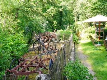 Historische landwirtschaftliche Maschinen neben einem grünen Garten mit Tischen und Sonnenschirmen.