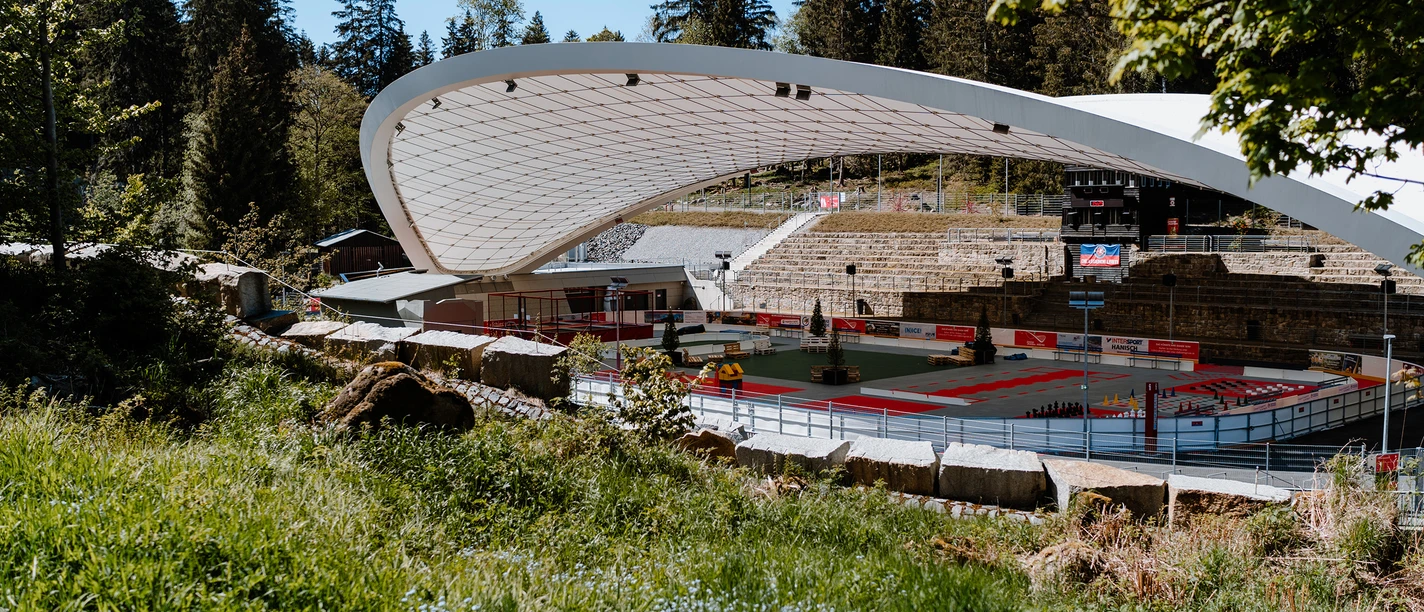 Schierker Feuerstein Arena mit geschwungenem Dach, Sportfläche und Waldkulisse.