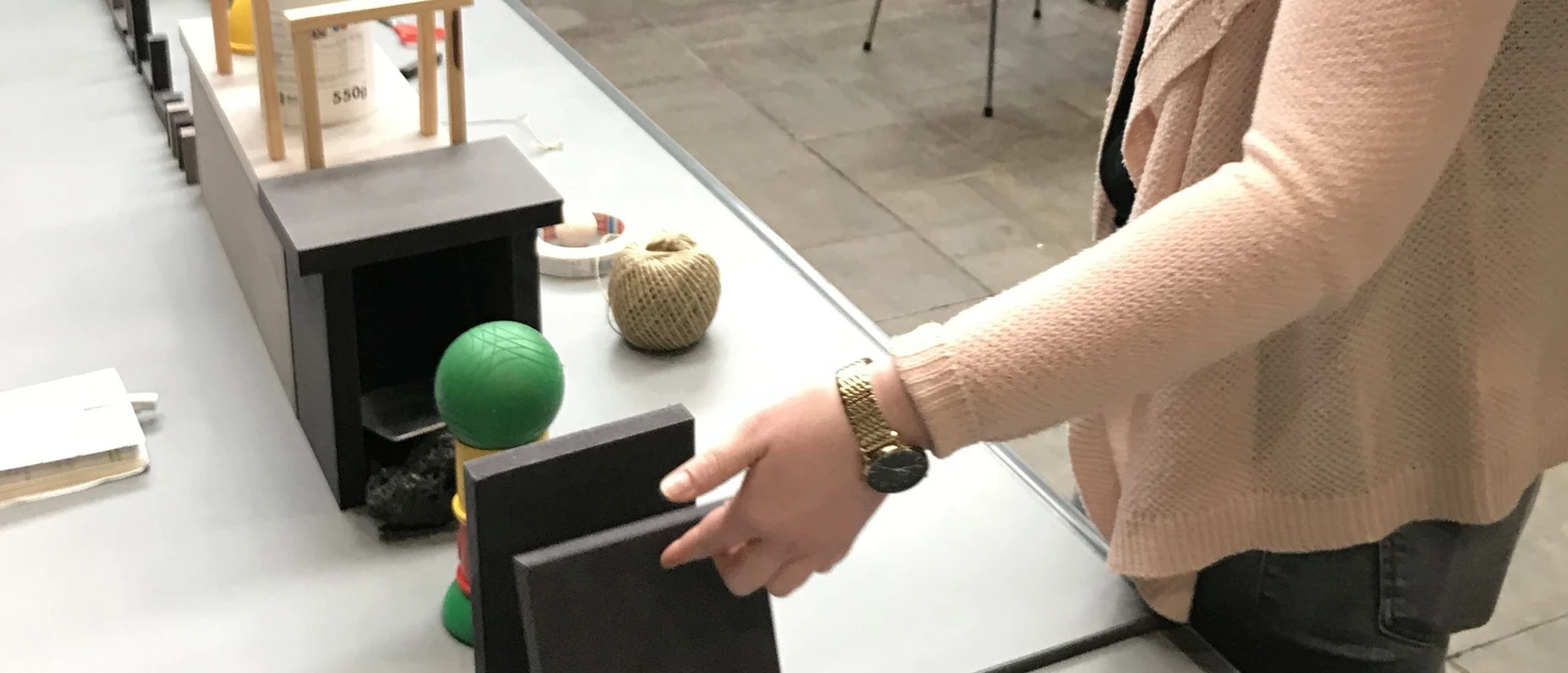Kettenreaktion Eine Person berührt architektonische Modelle auf einem Tisch in einer modernen, offenen Umgebung.
