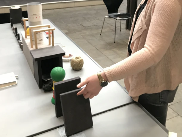 Kettenreaktion Eine Person berührt architektonische Modelle auf einem Tisch in einer modernen, offenen Umgebung.