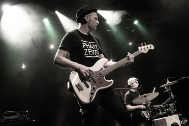 Platzkonzert_Phätte Zeiten 2.jpg Zwei Musiker spielen Gitarre und Schlagzeug auf einer Bühne, beleuchtet von Scheinwerfern.