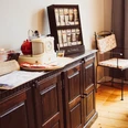cafe-harms-soderstorf1.jpg Holzschrank mit Teeauswahl, Retroradio und Speisekarte neben einem Tisch mit floraler Decke.
