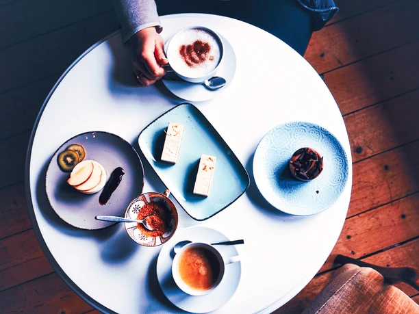 cafe-harms-soderstorf29.jpg Weißer runder Tisch aus der Vogelperspektive mit Kaffee, Kuchenstücken und Törtchen auf Tellern.