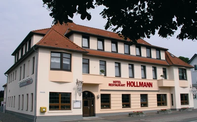 Das Bild zeigt das Hotel Restaurant Hollmann, ein dreigeschossiges Gebäude mit beige-weißer Fassade.