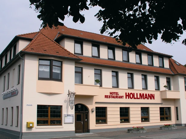 Das Bild zeigt das Hotel Restaurant Hollmann, ein dreigeschossiges Gebäude mit beige-weißer Fassade.