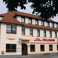 Hotelfront Das Bild zeigt das Hotel Restaurant Hollmann, ein dreigeschossiges Gebäude mit beige-weißer Fassade.