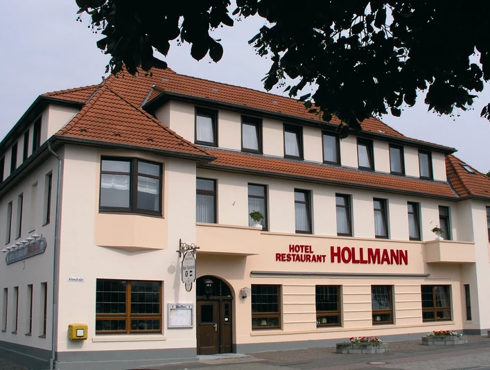 Hotelfront Das Bild zeigt das Hotel Restaurant Hollmann, ein dreigeschossiges Gebäude mit beige-weißer Fassade.