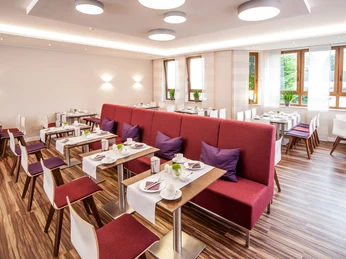 Restaurant mit modernem Interieur, rote Polsterbank, helle Holzmöbel, gedeckte Tische, Fenster.