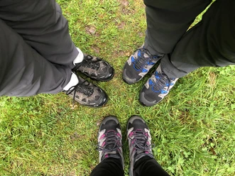 Drie paar wandelschoenen staan op een groene weide, klaar voor een buitenavontuur.