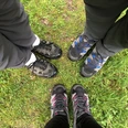 Drei Paar Wanderschuhe stehen auf grüner Wiese, bereit für ein Abenteuer im Freien.