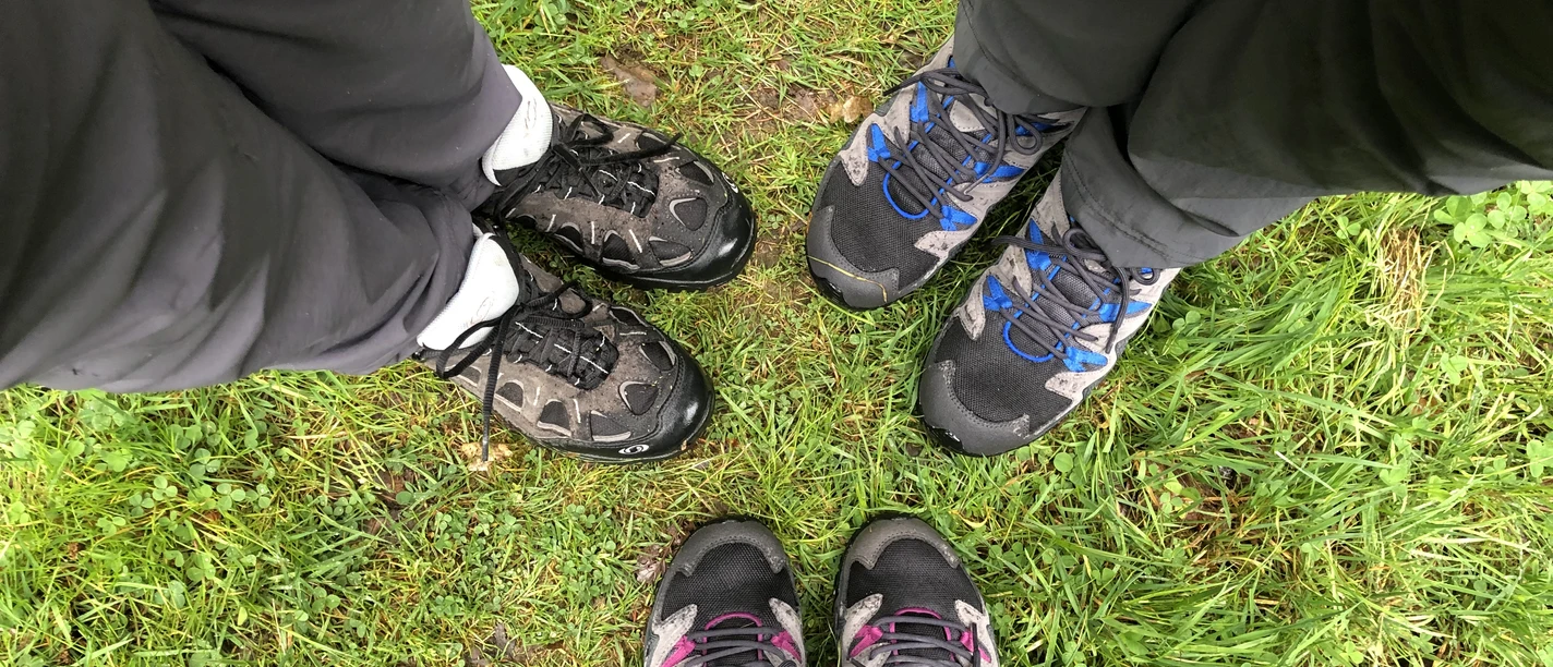 Wandern Drei Paar Wanderschuhe stehen auf grüner Wiese, bereit für ein Abenteuer im Freien.