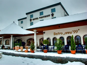 DSC_7636_7_8Enhancer-1.jpg Ein verschneites Gebäude mit dem Schild "Hotel Westhoff" neben einem Bistro. Pflanzen säumen den Eingangsbereich.