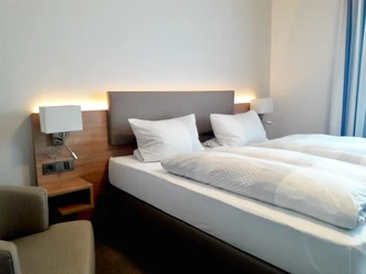 Helles Schlafzimmer mit einem Doppelbett, modernen Leuchten und einem Sessel in der Ecke.