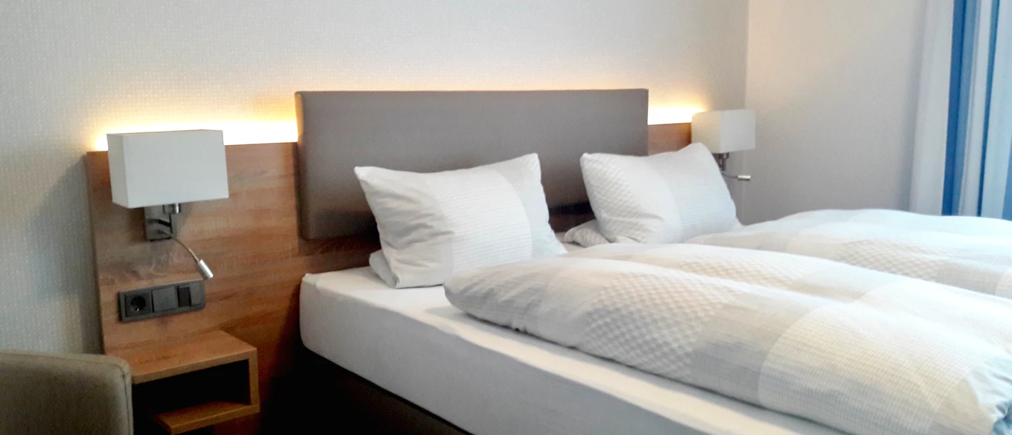 Schlafzimmer © Pension Dirkschnieder.jpeg Helles Schlafzimmer mit einem Doppelbett, modernen Leuchten und einem Sessel in der Ecke.