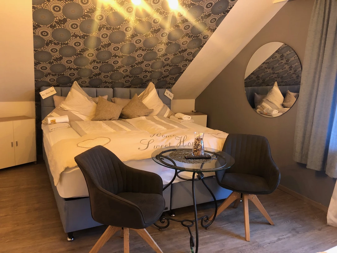 Dreibettzimmer mit Doppelbett, gemütlichen Kissen, zwei Stühlen und einem kleinen runden Tisch.