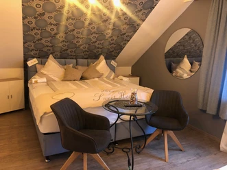 Pension © Ottenheide (1).jpeg Dreibettzimmer mit Doppelbett, gemütlichen Kissen, zwei Stühlen und einem kleinen runden Tisch.