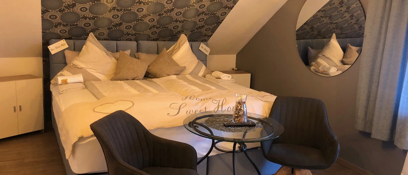 Pension © Ottenheide (1).jpeg Dreibettzimmer mit Doppelbett, gemütlichen Kissen, zwei Stühlen und einem kleinen runden Tisch.