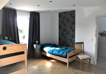 Apartment_Cosy_b_7439.JPG Helles Zimmer mit zwei Holzbetten, einem Stuhl und einem Fenster, das Licht auf den Holzboden wirft.