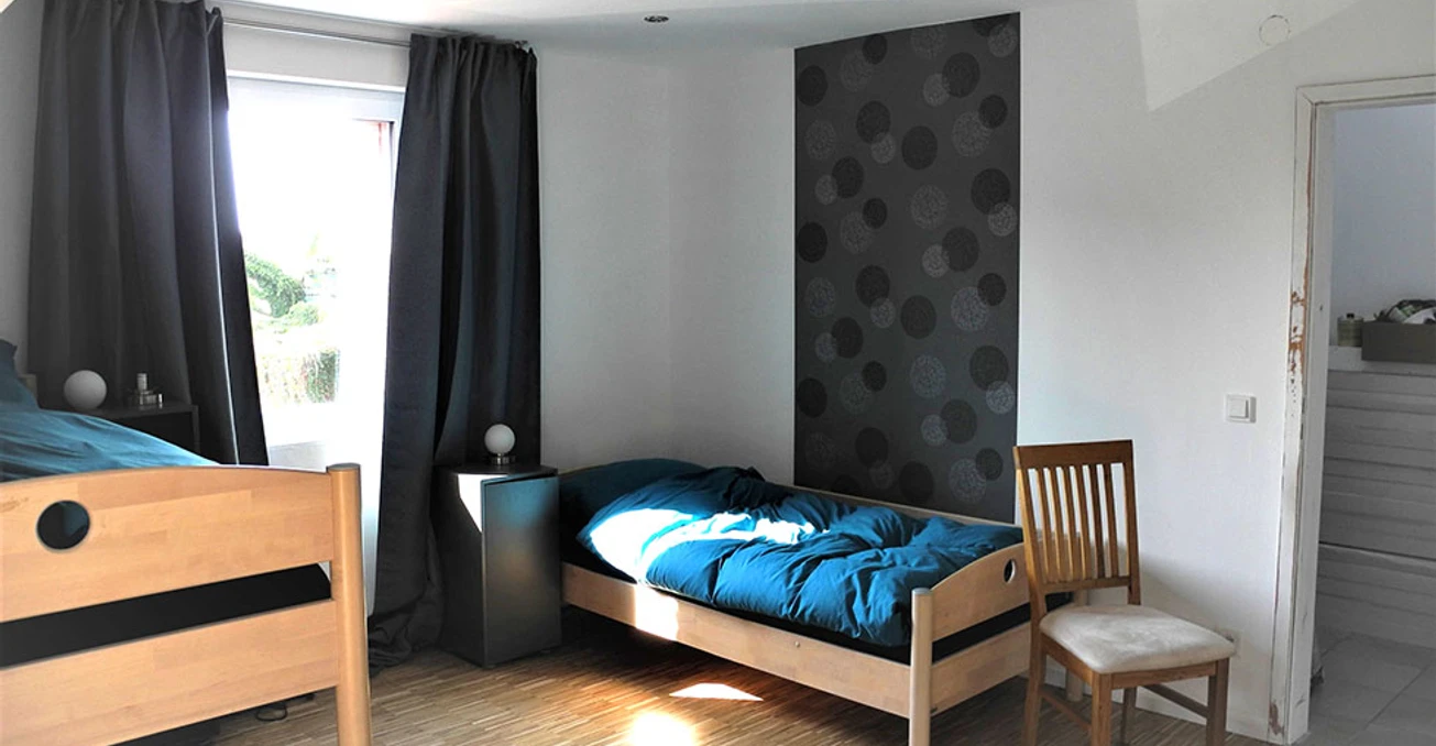 Apartment_Cosy_b_7439.JPG Helles Zimmer mit zwei Holzbetten, einem Stuhl und einem Fenster, das Licht auf den Holzboden wirft.