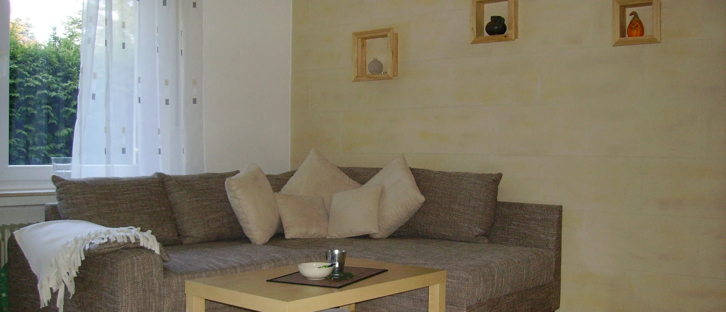 Gemütliches Wohnzimmer mit einer braunen Eckcouch, heller Wandfarbe und Holzmöbeln ausgestattet.