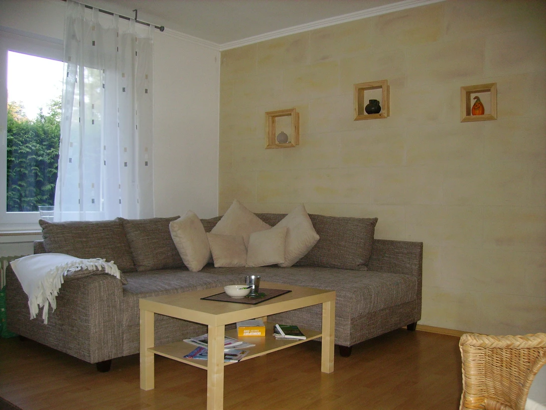 FeWo_ am Bokelfenn 001_c_SHS.jpg Gemütliches Wohnzimmer mit einer braunen Eckcouch, heller Wandfarbe und Holzmöbeln ausgestattet.