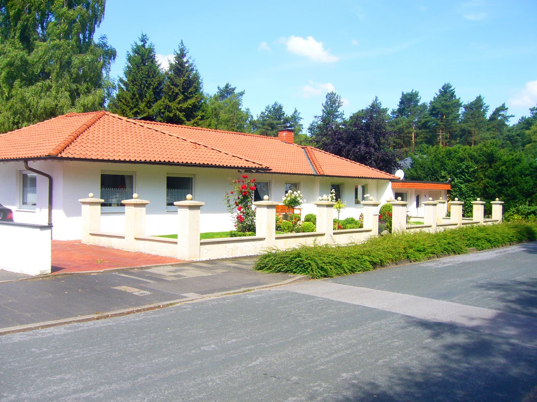 Forthof.JPG Ein eingeschossiges Haus mit rotem Ziegeldach umgeben von gepflegtem Garten und weißem Zaun.
