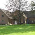 FeWo Stallmanns Hof.jpg Backsteinhaus mit Satteldach auf grünem Rasen, umgeben von Bäumen, Vorderseite mit Eingangstür