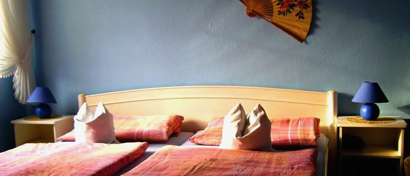 Ein Doppelbett mit rosa Bettwäsche, flankiert von blauen Lampen und asiatischen Fächern an der Wand.