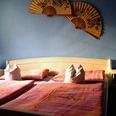 Pension_Sennetreff__StadtSHS.JPG Ein Doppelbett mit rosa Bettwäsche, flankiert von blauen Lampen und asiatischen Fächern an der Wand.