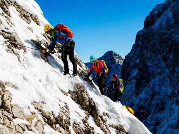 Zugspitze via Höllental (67 von 77).jpg Kletterer in bunter Ausrüstung besteigen ein schneebedecktes Bergmassiv bei strahlend blauem Himmel.