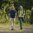 Zwei Wanderer schlendern entlang eines Waldweges, umgeben von Wacholderheiden im Teutoburger Wald.